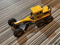 Side angle view of the yellow Tonka die cast plow showing tires, cab, and articulated blade.