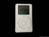 First generation Apple iPod powered on, screen showing ‘Now Playing’ song ‘Turn Off The Light’ by Nelly Furtado playing. Circular click wheel clearly visible. Screen is monochrome.