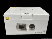 Box of Nikon 1 J1 digital camera with image of camera and lens printed on the box