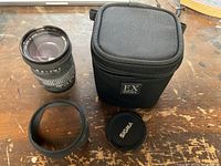 Top view of Sigma lens, soft case, lens hood, front cap, and rear cap displayed on wooden surface