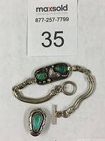 Photo of Navajo bracelet with green turquoise stones, silver detailed work, and attached chain clasp with round ring.