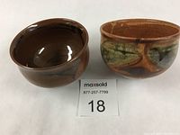 Two porcelain bowls side by side with lot number tag in front. One bowl glazed dark brown and black, other speckled brown with green accents.