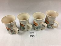 Front view of four ceramic mugs showing floral hand-painted orange poppies and green leaves on cream-colored background.