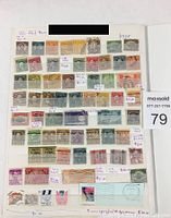 Photo showing a collection of older US postage stamps arranged on an album page. Many stamps have cancellation marks and varying values noted on small attached labels.