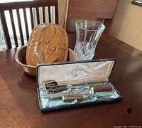 Photo showing the glazed Claybaker vase with embossed wheat and poppies design behind the boxed Sheffield carving set with bone handles, displayed on a wooden table.