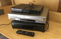 Photo of four electronic devices stacked: Bell TV receiver box on top, Panasonic 4-head Hi-Fi VCR underneath, Bell black device below with remote control in front.