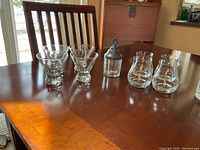 Photo shows 4 stemless wine glasses, 4 heavy bottomed dessert glasses, and 1 vintage glass jar with a pewter top on a wooden table.