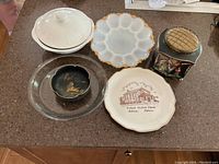 Photo showing six assorted glassware and ceramic items including lidded ironstone bowl, scalloped milk glass egg tray, Asian bowls, commemorative plate, and Pyrex pie plate.