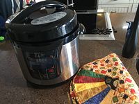 Electric pressure cooker with digital display and controls shown next to two colorful homemade fabric placemats on kitchen counter.