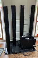 Four tall black Sony standing speakers and a black rectangular base unit with power adapter and cables arranged on the floor.