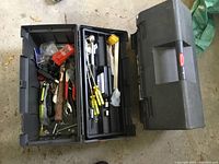 Photo of two black Rubbermaid tool boxes open and closed. Inside are various hand tools including hammers, pliers, screwdrivers, nails, screws, and other small tools and hardware.