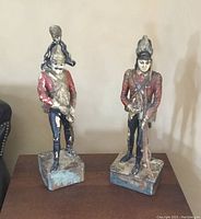 Pair of vintage hand-carved wooden soldier figurines standing on square bases, painted in red, black, and blue, showing detailed carving and paint wear