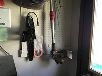 Photo showing Craftsman string trimmer hanging on wall with red and black handle, shield near cutting head, and a Mastercraft electric chainsaw hanging with power cord and handle. Also visible is a package of replacement orange trimmer line.