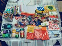Wide shot of assorted craft items laid out on a table including beads, tissue paper, thread, fabric, ribbons, and packaged craft materials.