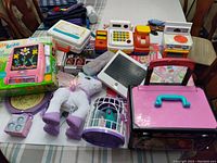 Photo showing a collection of girls toys including Lite-Brite set, plush unicorn, bird cage toy, electronic cash register, toy stove, pink suitcase, and small accessory toys.