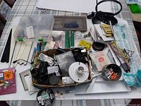 Overhead view of assorted hardware items laid out on a table, including electrical cords, lighting fixtures, various metal parts, wiring, and hand tools.