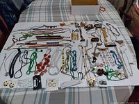 Photo showing assorted jewelry and fashion accessories laid out on a fabric surface including necklaces, bracelets, earrings, brooches, and pendants.
