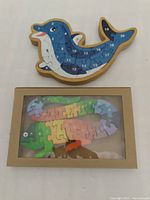 Dolphin and iguana wooden puzzles placed side by side, showing the iguana puzzle partly in the box and dolphin puzzle assembled.