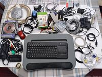 Overview of lot with the Logitech wireless keyboard on lap desk, multiple cables, power supplies, mice, numeric keypad, multi USB hub and other accessories