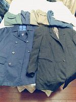 Photo showing five pairs of men's pants in green, tan, blue, beige colors with two jackets laid underneath on bed.
