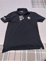 Front view of the black Edmonton Oilers polo shirt laid flat showing the overall condition, tags attached, Edmonton Oilers logo patch on chest, and two arm patches (including American flag)