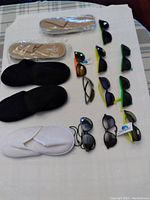 Top view of three pairs of spa/hotel slippers and ten assorted sunglasses arranged neatly on a white surface.