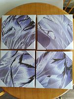 Full set of four canvas prints arranged on a wooden table showing purple abstract art.