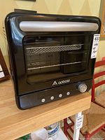 Front view of black Aobosi air fryer steam oven showing glass door with silver handle, control buttons and dial on bottom section, wire rack inside.