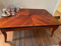 Full view of the rectangular wood coffee table showing patterned inlaid top, curved legs, and overall condition with some surface objects present.