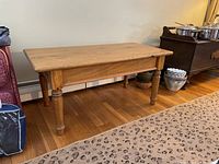 Full view of the rectangular wooden coffee table with turned legs and natural wood finish, showing its overall structure and condition.