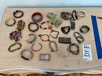 Wide view showing an assortment of 23 bracelets of various styles and materials laid out on a table.