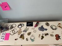 Wide view of assorted costume earrings and rings laid out on white surface showing different styles and materials