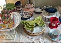 Overview of assorted dinnerware items including plates, bowls, mugs, and serving dishes on a white tablecloth