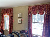 Window treatment setup showing two windows dressed with red and yellow patterned curtains and scalloped valances above them, hung on black curtain rods.