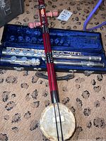 Photo showing the Gemeinhardt metal flute in its blue velvet-lined case alongside the red and black painted wooden string instrument with a drum-like body.