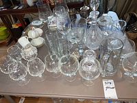Table with assorted clear glassware items including drinking glasses, goblets, a crystal decanter, and glass trinket boxes.