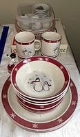 Full view of stacked holiday-themed plates, bowls, mugs, snowman figurine, and toy tea set on a table
