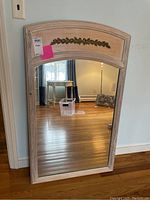 Full view of large rectangular wall mirror with light wood frame, arched top, and gold leaf decoration.