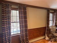 Two striped curtain panels hanging on windows with visible stripes of brown, tan, and beige. Curtain rods and wooden window frames also visible.
