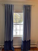 Light blue insulated curtains with navy trim on curtain rod hung over window, showing pleated hanging style and length.