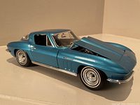 Side angled view of the metallic blue 1965 Chevrolet Corvette die-cast model car with the hood open, showing engine details and chrome wheel rims.