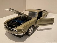 Front view of gold 1968 Mustang Mach 1 die-cast model with open hood showing detailed engine and open driver side door showing interior.