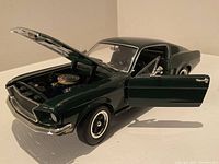 Front side view of dark green die-cast 1968 Ford Mustang Fastback model with hood and driver door open, showing detailed engine and interior.