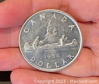 Reverse of the 1954 Canadian Silver Dollar showing a Voyageur and Indigenous person in a canoe, date 1954, and the word CANADA DOLLAR.