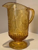 Front and side view showing amber glass pitcher with detailed relief including male bust portrait and soldier figure