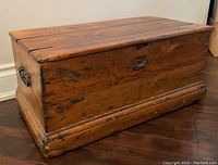 Full view of antique wooden chest closed, showing wood grain, metal handles on sides, and natural wear marks
