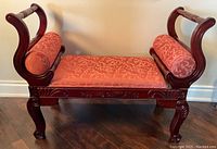 Front view of the carved wooden bench with upholstered seat and bolsters