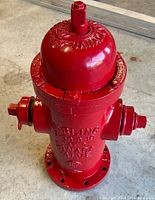 Top/front view of red powder-coated fire hydrant showing dome, outlet caps, base flange holes
