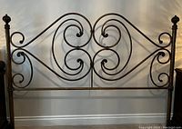 Front view of the metal headboard with intricate scroll design and finials on posts.