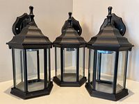 Front view of all three black metal hexagonal exterior wall-mounted house lights with glass panels.